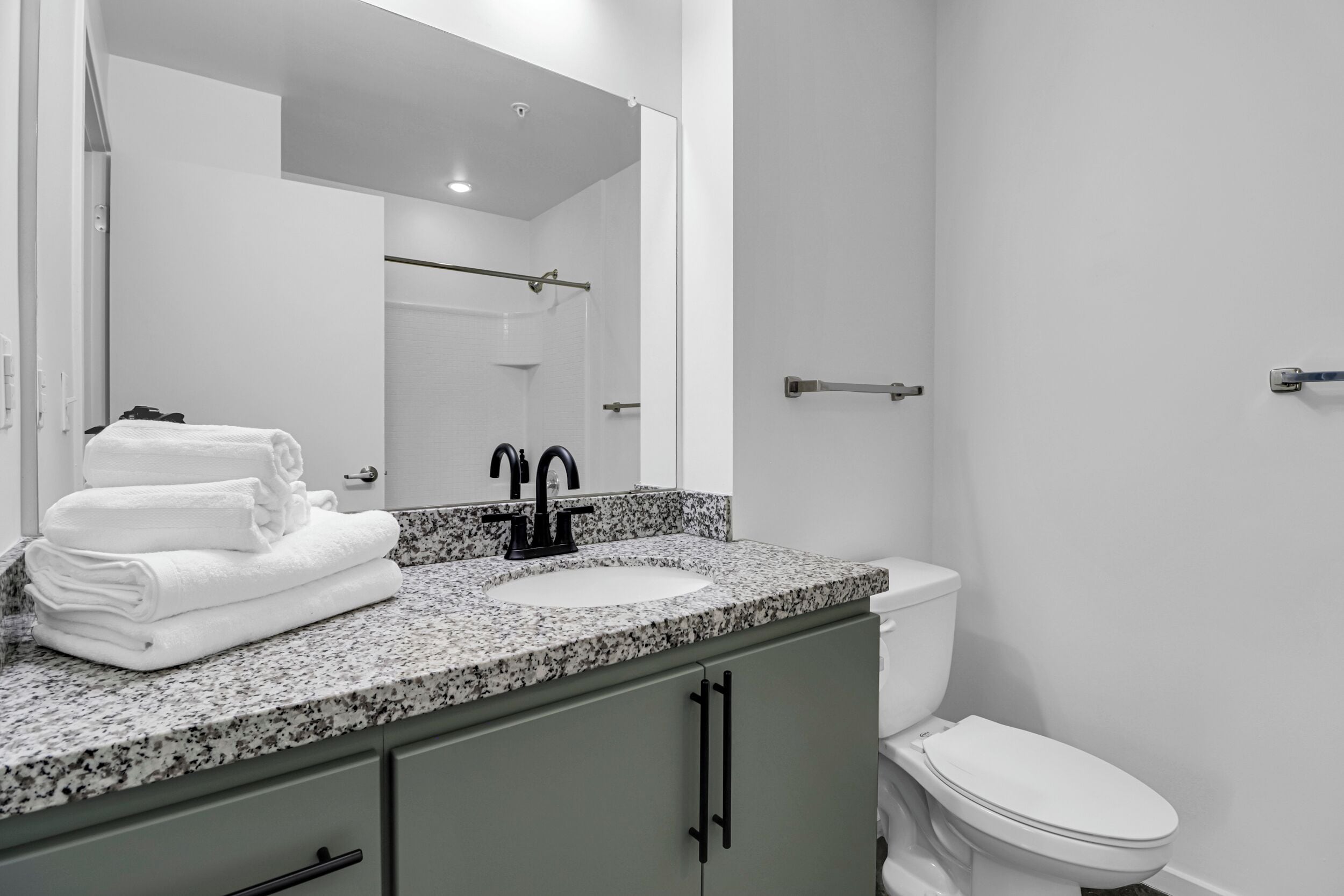 A bathroom with a granite countertop sink, a mirror, a toilet, and a towel rack.