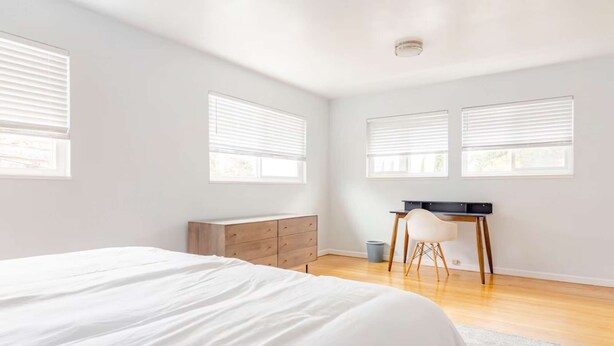 Un dormitorio con cama, cómoda, escritorio y dos ventanas.