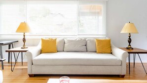 Una sala de estar con un sofá, dos lámparas, una mesa y una ventana con persianas.