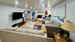 Una sala de estar moderna con un televisor de pantalla plana, una chimenea y un ventanal con persianas.