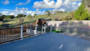 Una terraza de madera con barandilla metálica, un cobertizo pequeño y un área cercada con un área verde de césped.