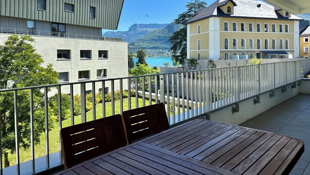 A balcony with a table and chairs, overlooking a scenic view of a lake and buildings.