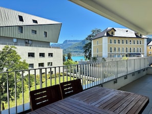 Un balcón con mesa y sillas, con vistas a un paisaje que incluye un lago y edificios.