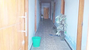 A hallway with wooden doors, a green basket, and a potted plant. - Kos Mama Ros (Labuan Bajo)