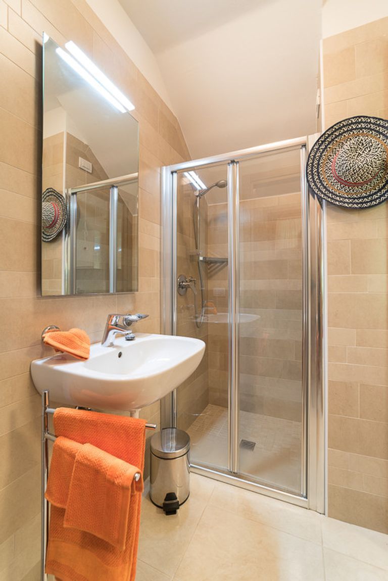 A bathroom with a glass shower enclosure, a sink with an orange towel, and a mirror.