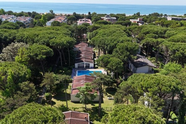 A coastal property with a row of villas, a central swimming pool, and dense surrounding trees.