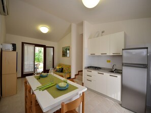 A compact kitchen with white cabinets, a stainless steel refrigerator, and a dining area with a table set for two.