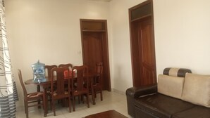 A dining area with a wooden table and chairs, a water dispenser, and a brown leather sofa. - Lovely 2-bedroom apartment with WiFi in vibrant Kigali (Kigali)