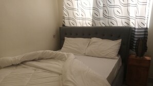 A bed with white bedding, a grey upholstered headboard, and a wooden nightstand with a lamp. - Lovely 2-bedroom apartment with WiFi in vibrant Kigali (Kigali)