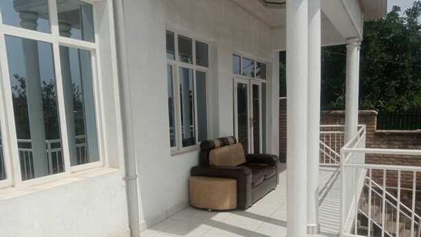 A covered outdoor area with a white railing, a brown and black sofa, and a window with a view of trees. - Lovely 2-bedroom apartment with WiFi in vibrant Kigali (Kigali)