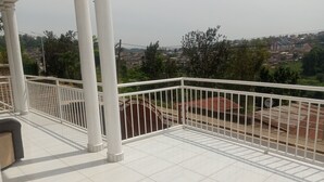 A balcony with white railings and a tiled floor, overlooking a residential area with houses and trees. - Lovely 2-bedroom apartment with WiFi in vibrant Kigali (Kigali)