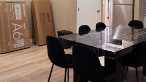 Un coin repas avec une table à plateau en verre et des chaises noires, entouré d’un parquet en bois et d’une porte blanche.