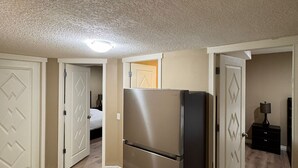 Une cuisine compacte dotée d’un réfrigérateur en acier inoxydable, d’un plancher en bois et de portes blanches ornées de motifs en losange.