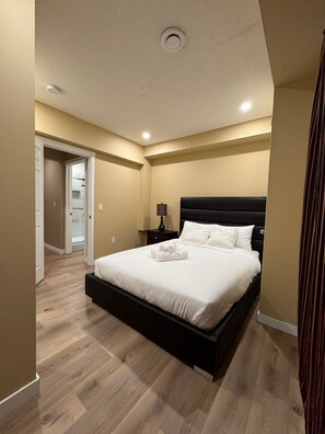 A modern bedroom with a large bed, a nightstand, and a ceiling light. - Spacious 4BR Basement Suite in Calgary (Calgary)