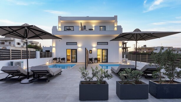 Un área moderna de piscina en la azotea con sillones de descanso y sombrillas, piscina y un edificio con varios pisos y balcones.