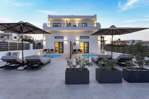 Un espace piscine moderne aménagé sur le toit, avec des chaises longues et des parasols, une piscine, et un immeuble à plusieurs étages doté de balcons.