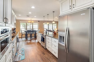Una cocina amplia con electrodomésticos de acero inoxidable, piso de madera y un comedor con candelabro.