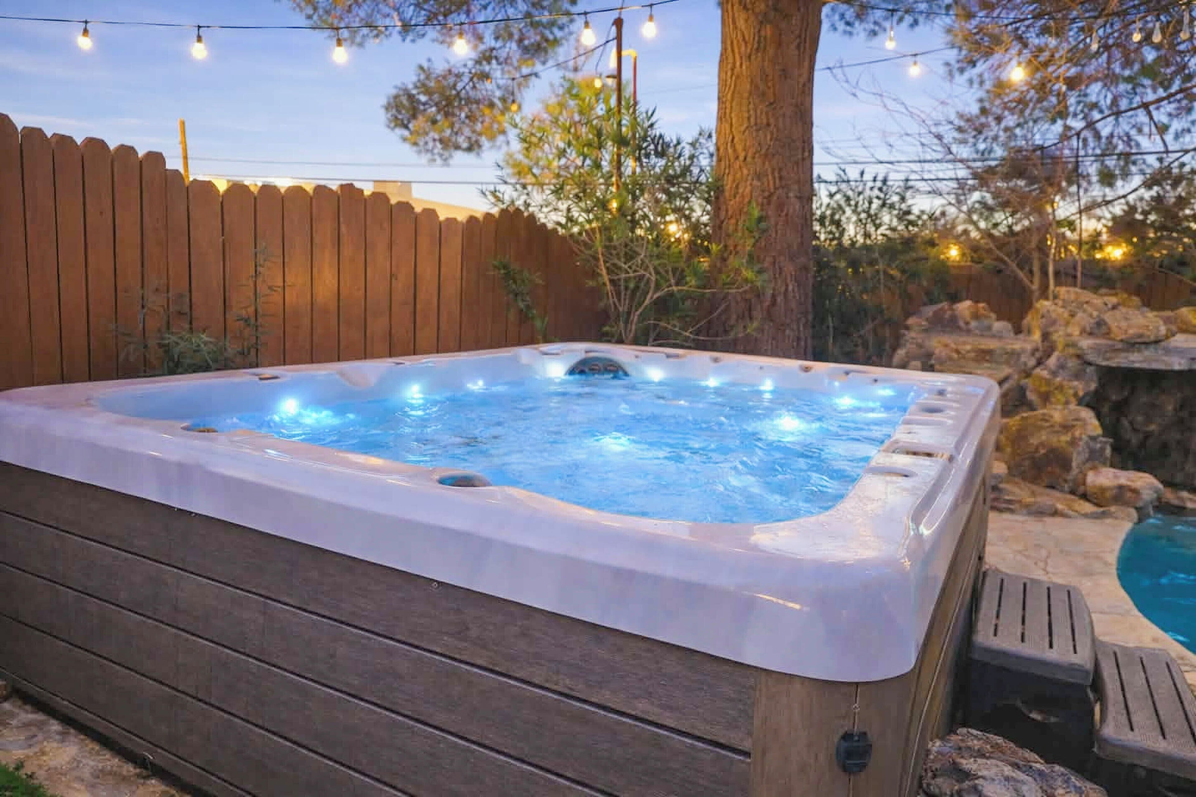 A hot tub with a wooden deck, surrounded by a wooden fence, and string lights above.