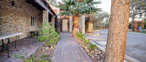 A brick building with a paved walkway, palm trees, and a bench.