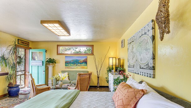 Una habitación con cama, una silla, un escritorio, una ventana y un cuadro en la pared.
