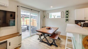 A modern kitchen with a wooden table, white cabinets, and a sliding glass door leading to an outdoor patio. - 2 Mi to Olympic National Park: Sun-soaked Haven! (Port Angeles)