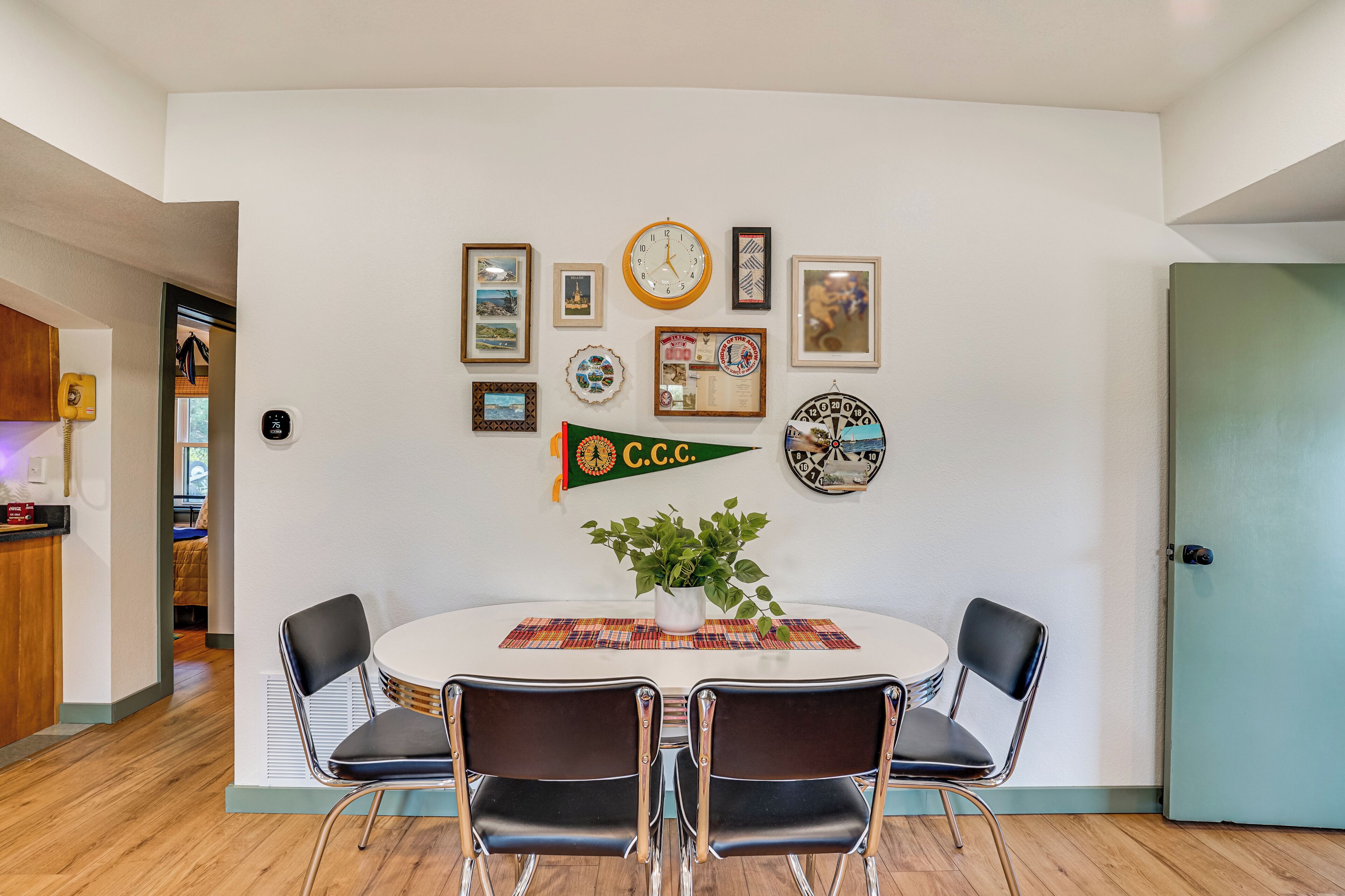 Un coin repas avec une table ronde, deux chaises, une horloge et divers tableaux encadrés accrochés au mur.