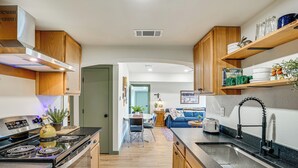 A modern kitchen with wooden cabinets, a built-in stove, a sink, and a dining area in the background. - Lake View + Huge Deck: Cozy Possum Kingdom Retreat (Graham)