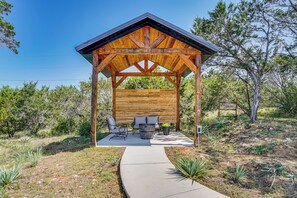 A wooden gazebo with a sloped roof, built-in seating, and a concrete pathway leading to it.