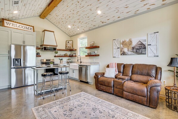 A spacious living area with a brown leather sofa, a kitchen with white cabinetry, and a 'WELCOME' sign on the ceiling.