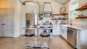 A modern kitchen with white cabinetry, a central island with stools, a stainless steel refrigerator, and a built-in oven. - Recently Built Cabin w/ Pavilion in Granbury! (Granbury)