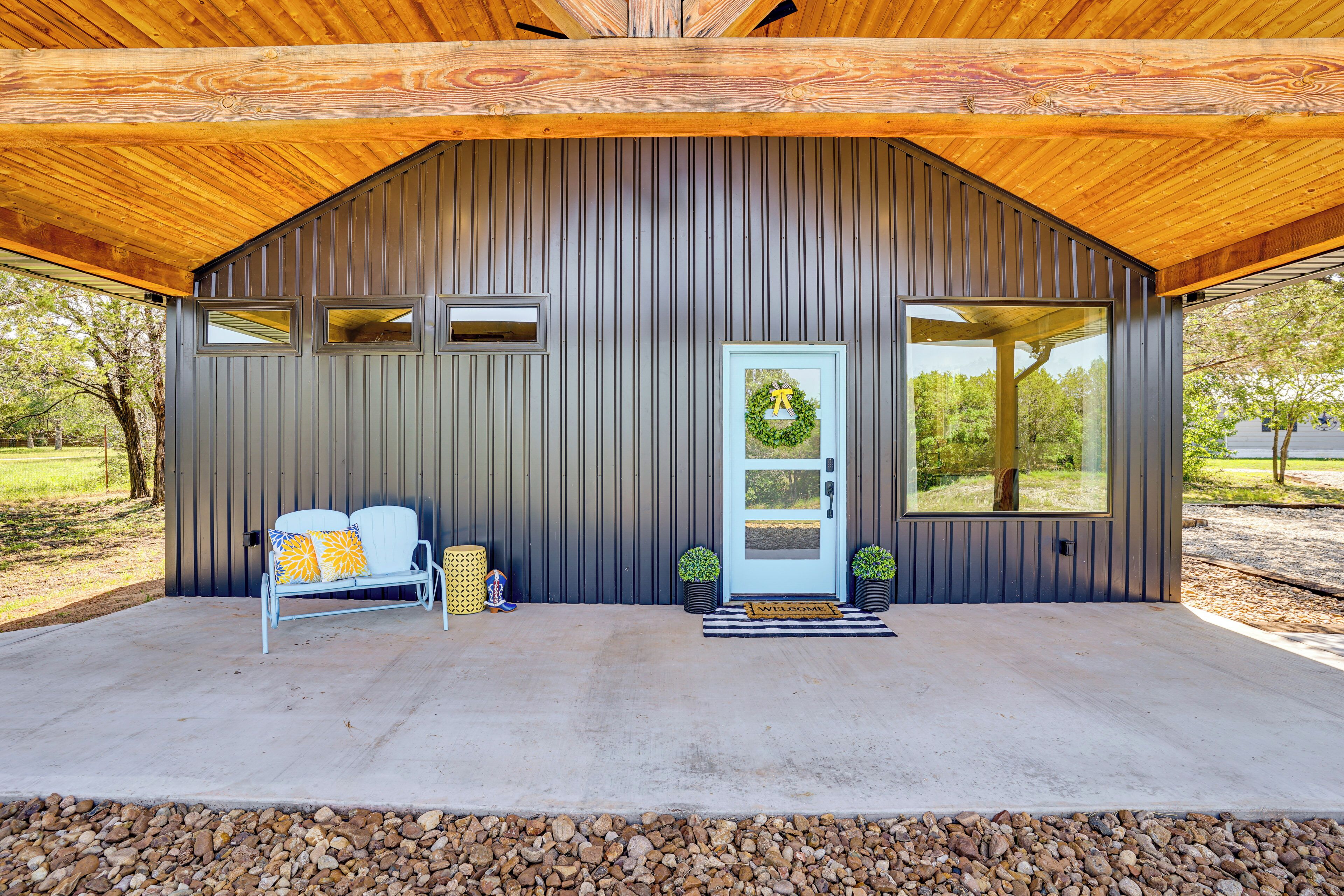 A modern building with a sloped roof, a front door with a wreath, a bench, and two potted plants.