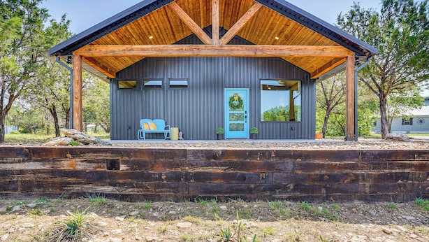 A rustic cabin with a wooden roof and a blue door, surrounded by trees and a wooden deck. - Recently Built Cabin w/ Pavilion in Granbury! (Granbury)