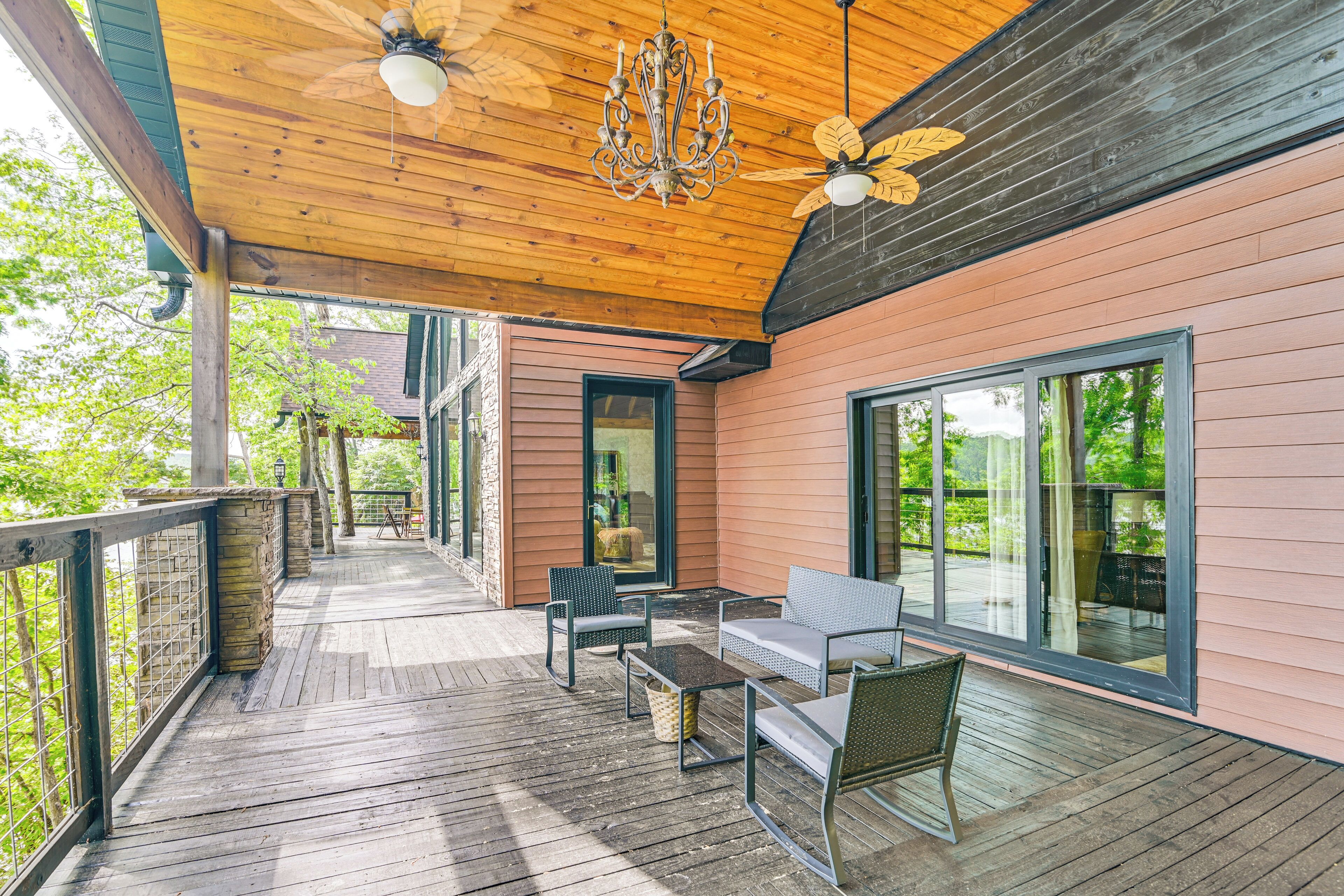 A wooden deck with outdoor furniture, large windows, and a ceiling fan.