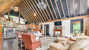 A spacious living room with a high ceiling, wooden beams, and a large fireplace. There are leather sofas and a dining area with wooden furniture. - Upscale Getaway on Smith Lake w/ Boat Dock (Houston)