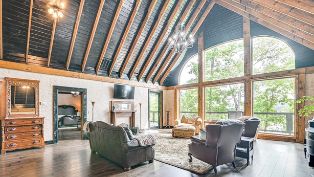 A spacious living room with a high ceiling, wooden beams, large windows, and a fireplace. - Upscale Getaway on Smith Lake w/ Boat Dock (Houston)