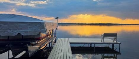 Un vehículo cubierto sobre un muelle de madera que se extiende hacia aguas tranquilas, con un banco y un poste de luz solar.