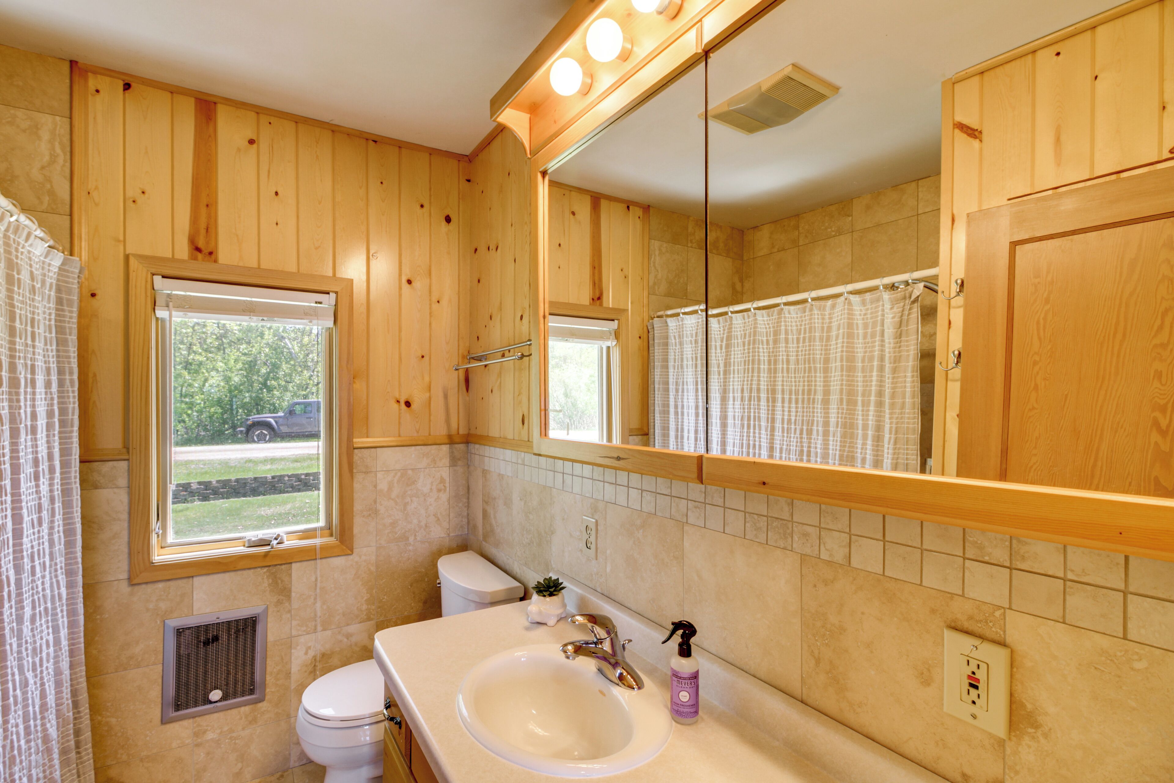 Une salle de bain aux murs lambrissés, avec une fenêtre, des toilettes, un lavabo et un miroir.