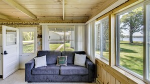 A cozy room with a grey sofa, two white cushions, and a view of a lake through large windows. - Hackensack Waterfront Retreat on Tenmile Lake (Hackensack)