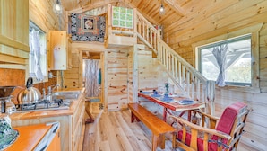 A wooden cabin interior with a kitchen, dining area, and a staircase leading to a loft. - 'fins & Flowers' Off-grid Cabin w/ Trout Fishing! (Lewiston)
