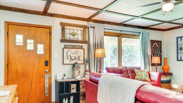 A cozy living room with a red leather sofa, wooden door, and a 'Make Yourself at Home' sign. - < 1/2 Mi to Lake: Secluded Gem in Cherokee Village (Cherokee Village)