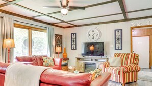 A living room with a red leather sofa, a striped armchair, a television, and a fireplace. - < 1/2 Mi to Lake: Secluded Gem in Cherokee Village (Cherokee Village)