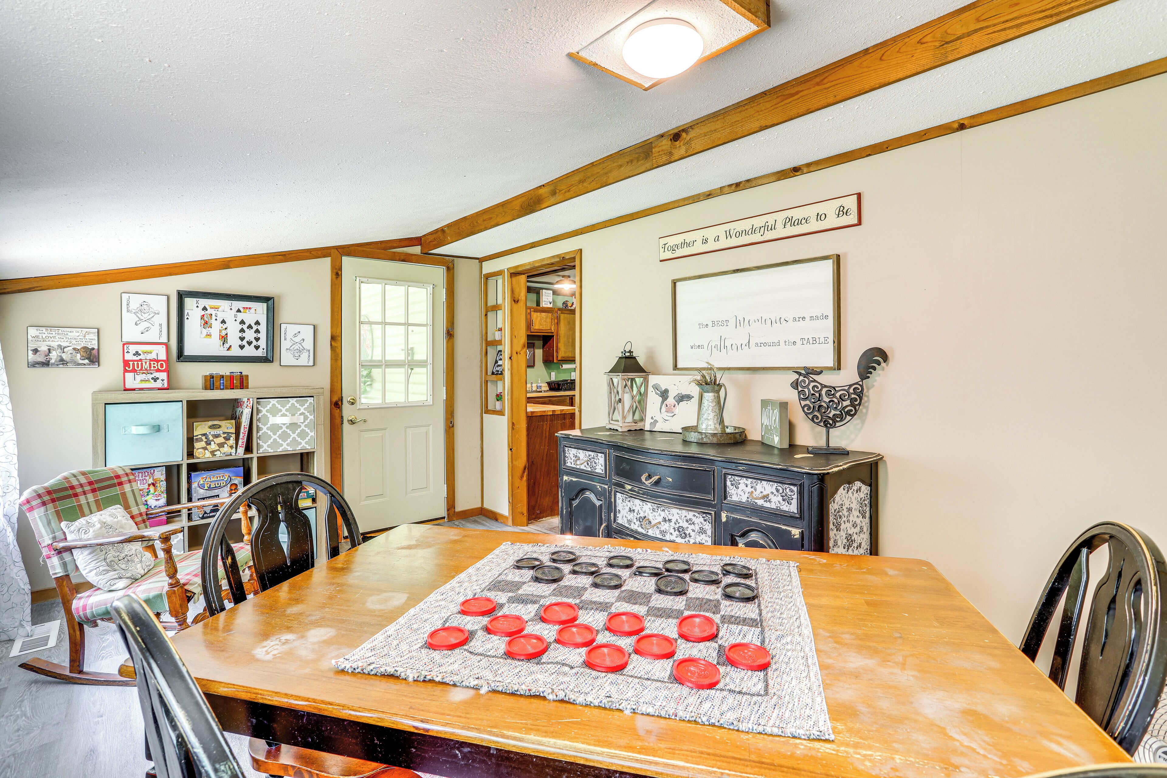 A dining area with a checkered tablecloth, wooden chairs, a rocking chair, a wooden cabinet, and a door leading to another room.