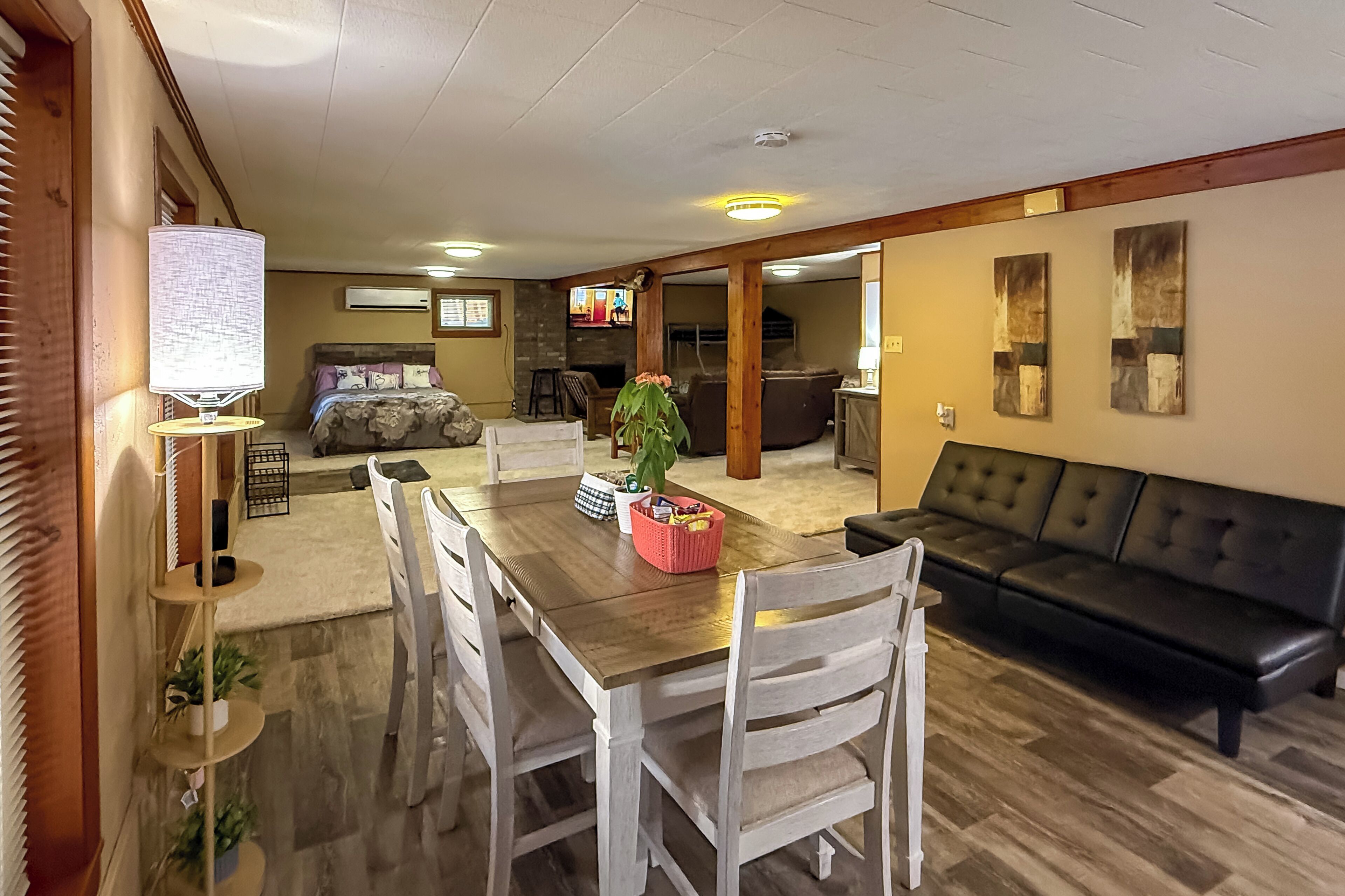 A spacious living room with a wooden dining table, white chairs, a black leather sofa, and a television.