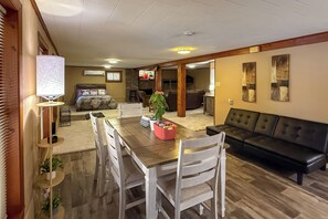 A spacious living room with a wooden dining table, white chairs, a black leather sofa, and a television. - Lakefront Retreat w/ Patio in Fort Towson! (Fort Towson)