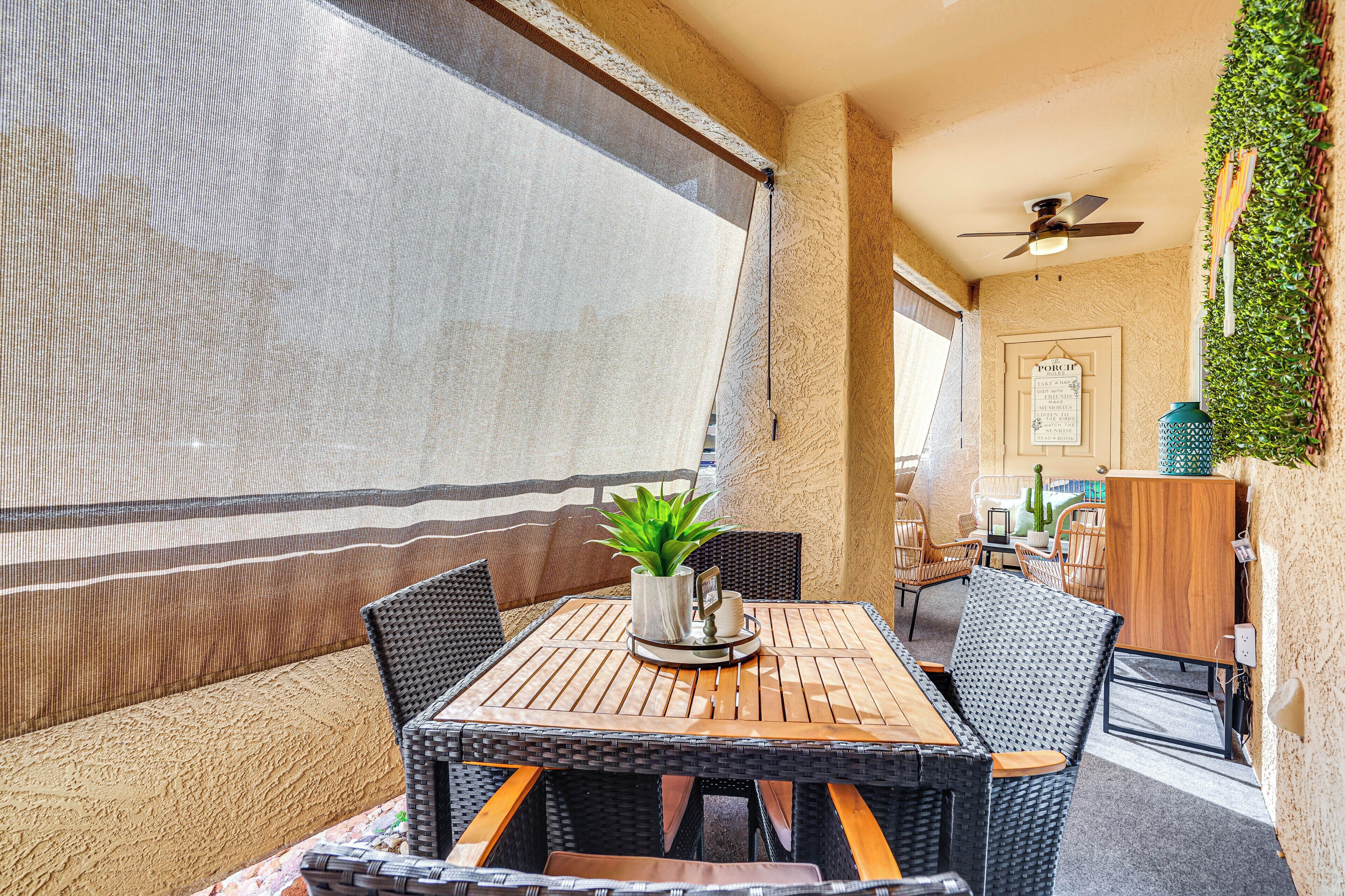 An outdoor patio with a table and chairs, a ceiling fan, and a wall with greenery.