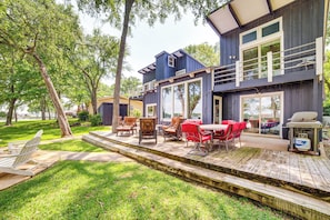 Ein zweigeschossiges Haus mit einer Terrasse, Sitzgelegenheiten und einem Grill.