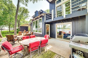 Eine Terrasses mit Esstisch und Stühlen, einem Grill und Blick auf einen See.