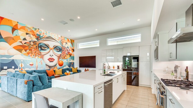 A modern kitchen with white cabinets, a central island, and a colorful mural on the wall.