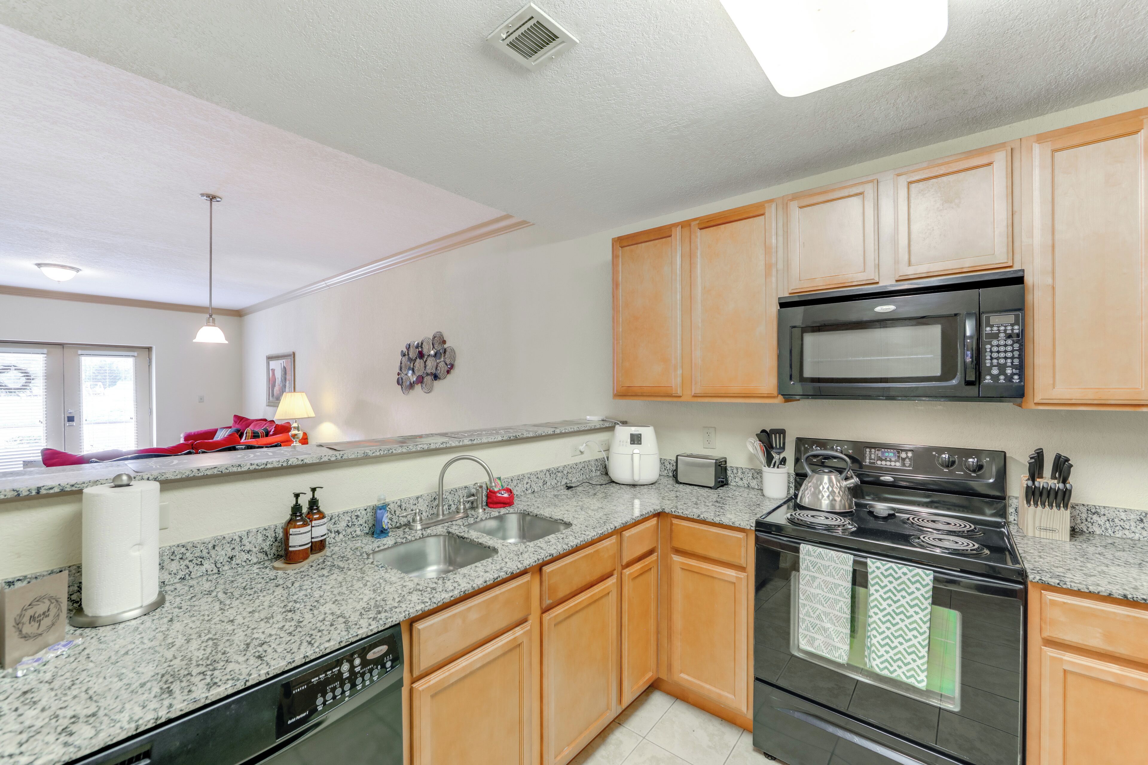 A modern kitchen with granite countertops, wooden cabinets, a black stove, a microwave, and a dishwasher.