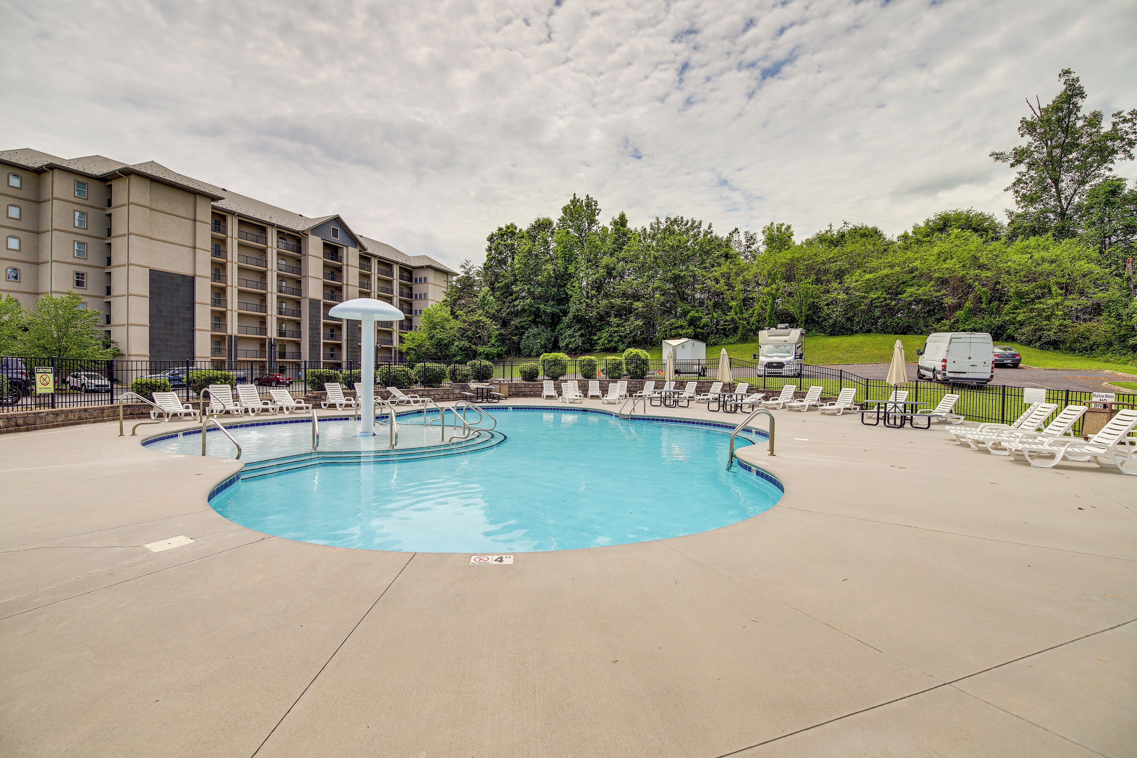 A swimming pool with lounge chairs and a covered area, surrounded by a fence and trees.